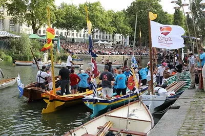 Au premier plan des petits bateaux s'arriment à quai. De l'autre côté de l'Erdre, des centaines de personnes sont assises pour assister à un concert des Rendez-vous de l'Erdre.