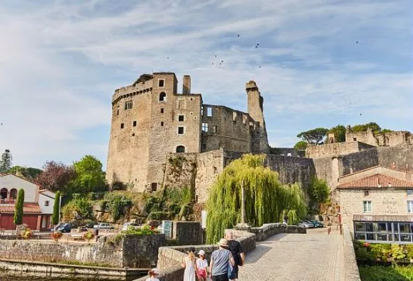 Une famille traverse le pont en pierre qui enjambe la Sèvre à Clisson. Devant elle se dresse le château de Clisson, Grand Patrimoine de Loire-Atlantique