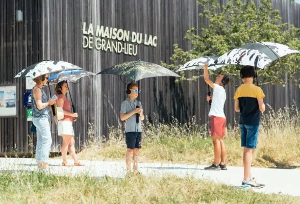 Sous des parapluies sonores, des personnes débutent la balade sonore qui mène du centre d'exposition au pavillon.