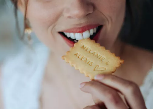 Une femme croque dans un biscuit petit beurre où il est inscrit "Mélanie & Alexis"