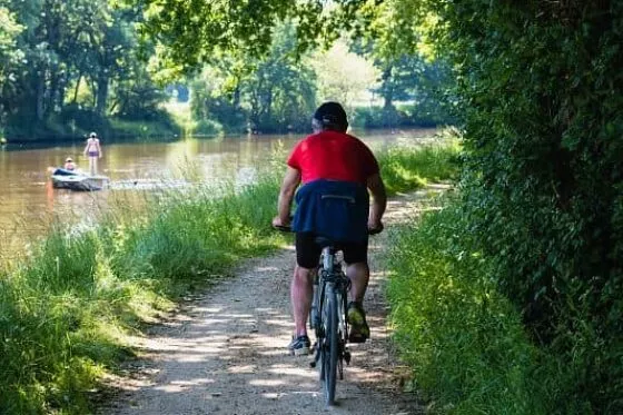 Un cycliste roule sur le chemin de halage du Canal de Nantes à Brest, à l'ombre des arbres