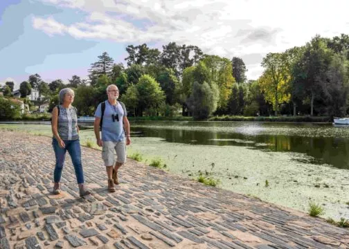 Un couple de seniors marche sur une route pavée bordée d'eau : la chaussée des Moines à Vertou
