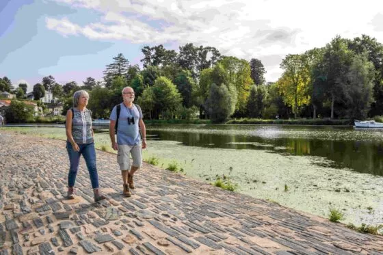 Un couple de seniors marche sur une route pavée bordée d'eau : la chaussée des Moines à Vertou