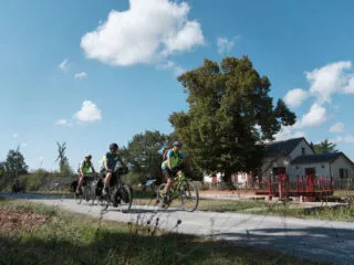 Trois cyclistes en itinérance roulent à côté d'une maison éclusière le long du Canal de Nantes à Brest