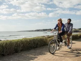 Une femme et un homme sur un tandem pédalent en bord de mer