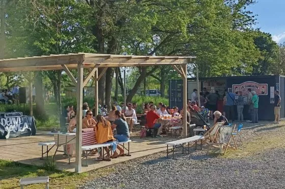 Vue sur la pergola de la guinguette des Janettes où des personnes se restaurent.