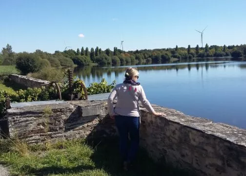 Une femme regarde une rivière, appuyée sur un muret