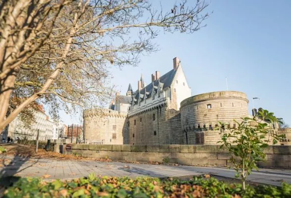 Le château des ducs de Bretagne : une enceinte médiévale entourée de douves avec un chemin de ronde et des meurtrières et au dessus un bâtiment du 15e siècle en pierre de tuffaut blanche.