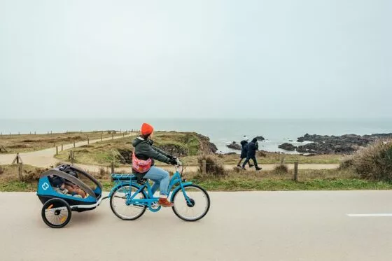 Un cycliste tirant une carriole pour enfant pédale en bord de mer