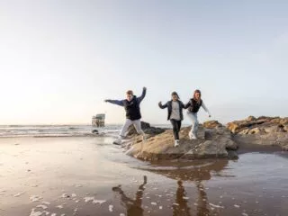 Trois jeunes sautent sur la plage de Saint-Brevin au soleil couchant. Derrière eux une pêcherie.