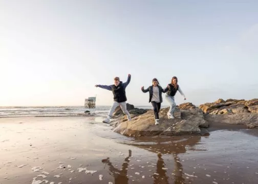 Trois jeunes sautent sur la plage de Saint-Brevin au soleil couchant. Derrière eux une pêcherie.