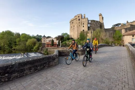 Des cyclistes sur un pont de pierres à Clisson, avec vue sur le château.