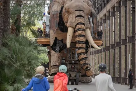 Trois cyclistes font face au Grand Elephant des Machines de l'Ile à Nantes.