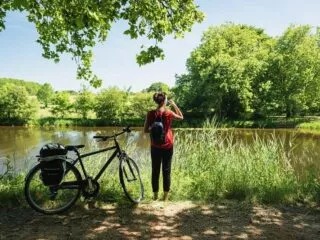 Une femme debout à côté de son vélo regarde le canal de Nantes à Brest en profitant de l'ombre des arbres