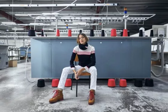 Une jeune femme pose dans un atelier, habillée en marinière et entourée de bobines de fils