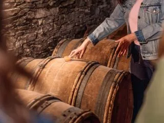 Une guide pose la main sur un tonneau de vin dans une cave du Vignoble