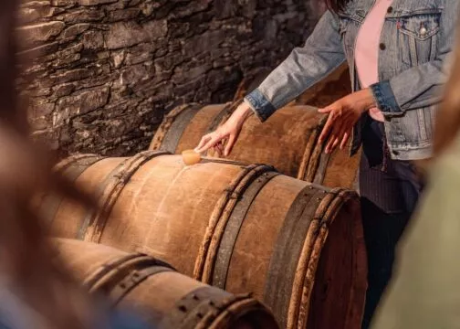 Une guide pose la main sur un tonneau de vin dans une cave du Vignoble