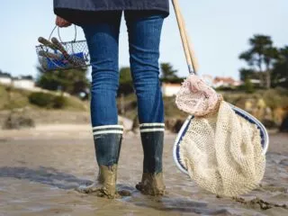 Une personne en botte de pluie se tient debout sur une plage, une épuisette à la main