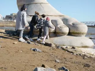 Une famille s'approche de la sculpture d'un pied géant, oeuvre du Parcours Estuaire