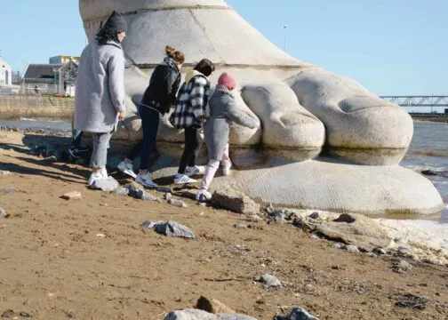 Une famille s'approche de la sculpture d'un pied géant, oeuvre du Parcours Estuaire