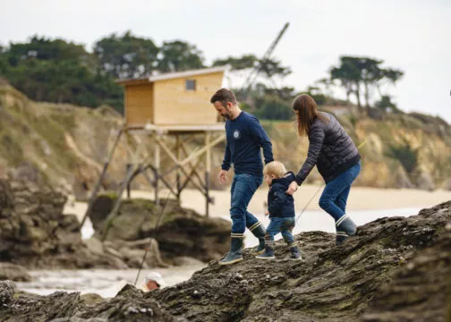 Deux parents se baladent avec leur jeune enfant sur les rochers avec une pêcherie en arrière-plan