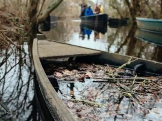 Une barque avec un peu d'eau et de feuille à l'intérieur, on devine un groupe sur une barque qui naviguent en arrière-plan