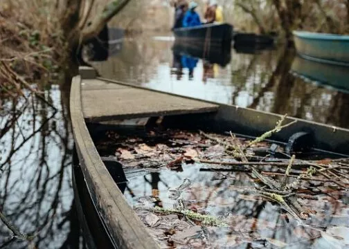 Une barque avec un peu d'eau et de feuille à l'intérieur, on devine un groupe sur une barque qui naviguent en arrière-plan