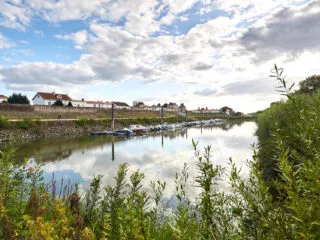 Vue sur les bords de Loire et la levée de la Divatte, bordée de maisons. Le ciel se reflète sur le fleuve qui est bordé de verdure.