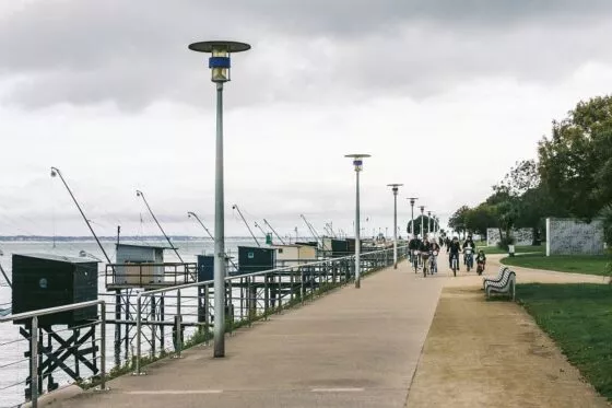 Des cyclistes sur le front de mer, circulent à côté de pêcheries sous un ciel gris.