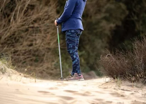 Une personne tenant son bâton de randonnée sur un sentier de sable