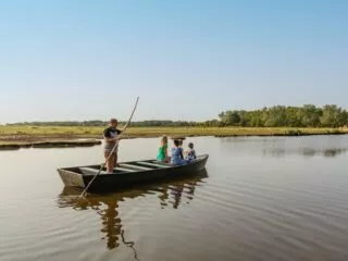 Un promeneur en chaland, perche à la main, promène dans son bateau à fond plat une famille dans le marais de Brière