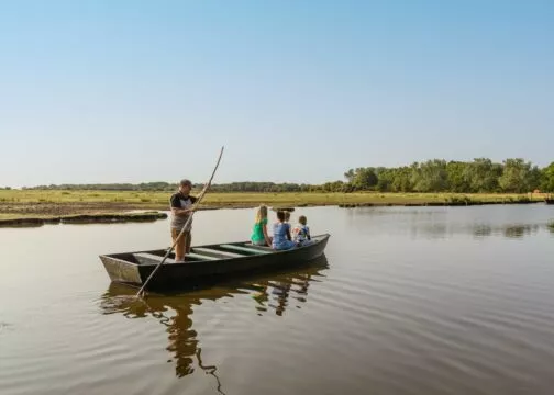 Un promeneur en chaland, perche à la main, promène dans son bateau à fond plat une famille dans le marais de Brière