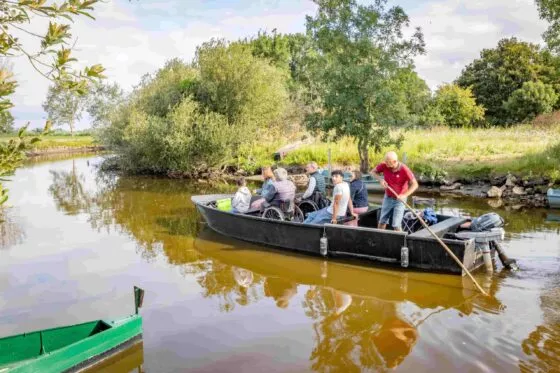 Un promeneur en chaland pousse sur sa perche pour faire avancer son bateau au départ du port de Rozé. Dans son chaland est installée une famille avec deux personnes en fauteuil roulant.