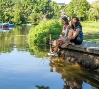 Deux jeunes femmes sont assises sur un ponton à l'ombre, au bord d'une rivière