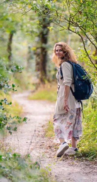 Une femme en robe d'été se retourne pour regarder ses deux adolescents qui marchent derrière elle sur un sentier dans une forêt